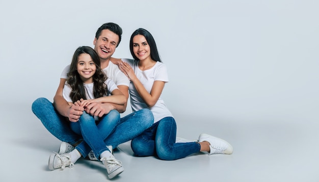 Mooi opgewonden en het grappige familieteam poseert in een wit t-shirt terwijl ze geïsoleerd op een witte achtergrond in de studio.