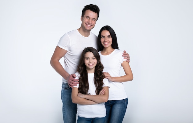 Mooi opgewonden en het grappige familieteam poseert in een wit t-shirt terwijl ze geïsoleerd op een witte achtergrond in de studio.