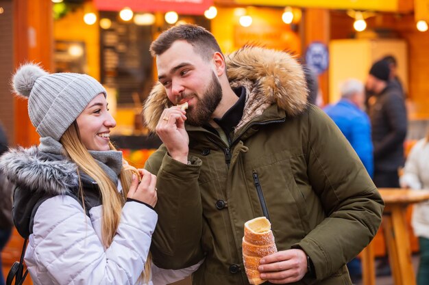 Foto mooi paar dat tsjechische trdelnik eet op kerstmarkt in wroclaw, polen