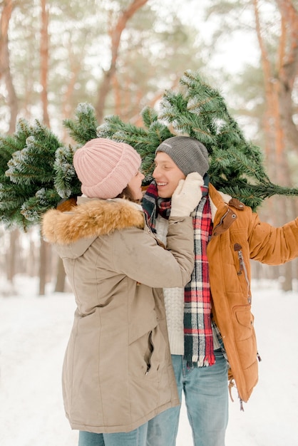 Mooi paar met een kerstboom in het besneeuwde bos