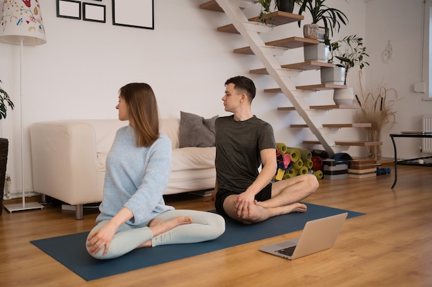 Mooi paar samen beoefenen van yoga thuis met behulp van een laptop met online yogalessen