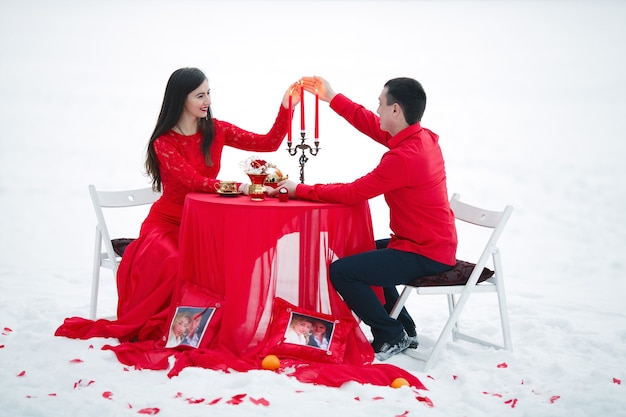 Mooi paar zittend aan een tafel met een kandelaar op een achtergrond van sneeuw in rode kleren