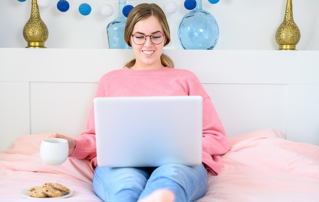 Mooi portret freelance jonge vrouw zitten ontspannen en vrije tijd werkende laptopcomputer internet online op bed in de slaapkamer, vrolijk meisje met gebaar blij en succes, lifestyle concept.