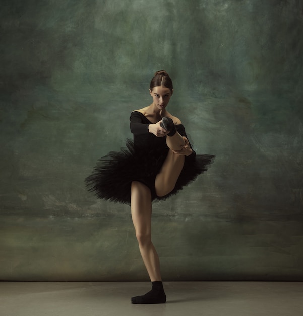 Mooi portret. sierlijke klassieke ballerina dansen, poseren geïsoleerd op donkere studio achtergrond. elegantie zwarte tutu. genade, beweging, actie en bewegingsconcept. ziet er gewichtloos uit. in de mode.