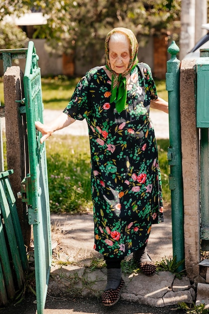 Mooi portret van een oudere vrouw gekleed in een badjas en sjaal die poseert voor een foto bij een oude boom in haar tuin