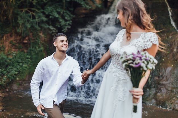 Mooi portret van mooie en jonge bruidegom en bruid staande op waterval