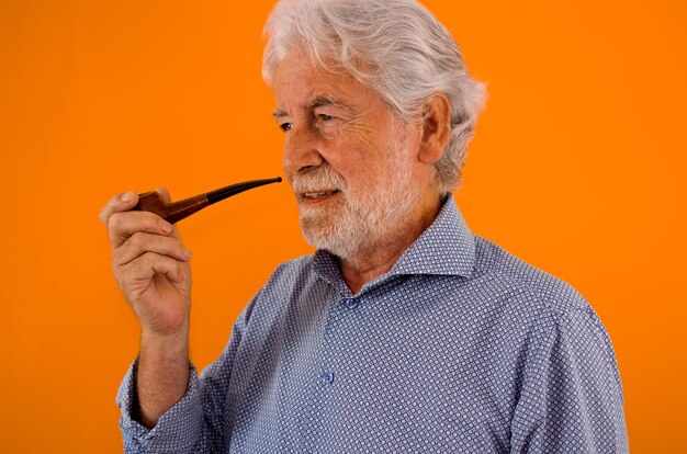 Mooi portret van senior bebaarde man rookpijp staande op oranje achtergrond