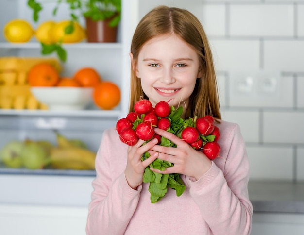 Mooi preteen meisje met jonge radijs in de keuken thuis en glimlachend Mooi vrouwelijk kind met gezonde eco-groenten