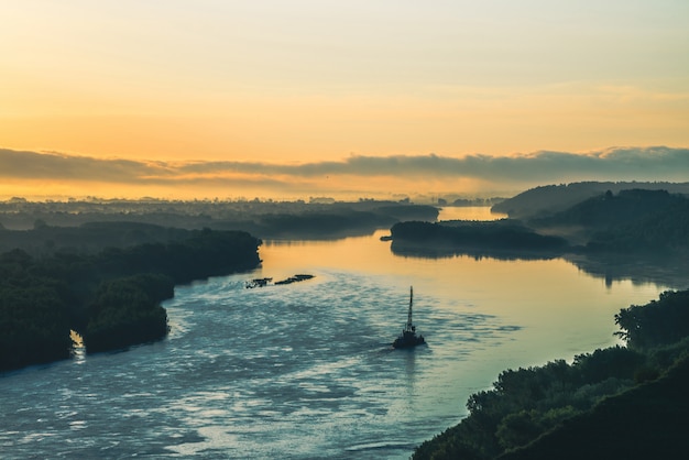 Mooi rivierlandschap met groene kusten en schip met exemplaarruimte. De sleepboot sleept aak met kraan langs rivieroever. Dawn gereflecteerd op kalm wateroppervlak.