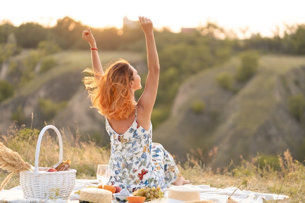 Mooi roodharig meisje geniet van de zonsondergang op de natuur. Picknick in het veld.