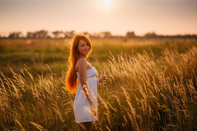 Mooi roodharig meisje in een veld bij zonsondergang