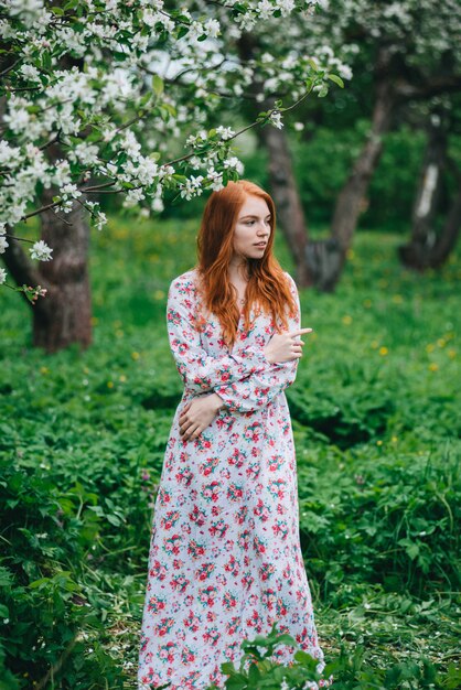 Mooi roodharig meisje in een witte jurk onder bloeiende appelbomen in de tuin