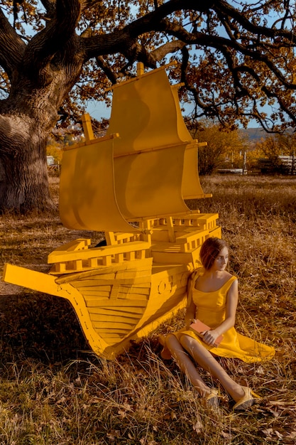 Mooi roodharig vrouwenportret met boek en schip dichtbij eikenboom in de herfst