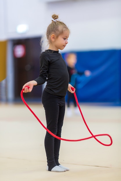 mooi schattig meisje loopt met een springtouw. Gelukkige jonge geitjes glimlachen en springen in de sportschool met spiegels. Ze droegen zwarte sportkleding. Kinderen leiden een gezonde levensstijl