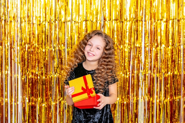 Mooi schattig vrolijk kindmeisje op een gouden vakantieachtergrond met een geschenkdoos in haar handen