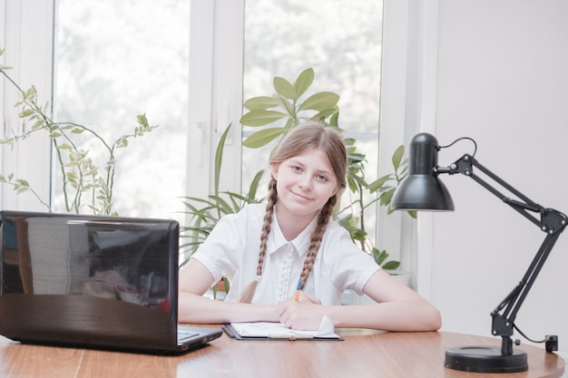 Mooi schoolmeisje dat huiswerk bestudeert tijdens haar online les thuis, sociale afstand tijdens quarantaine, zelfisolatie, online onderwijsconcept, thuisschooler. Online onderwijs op afstand