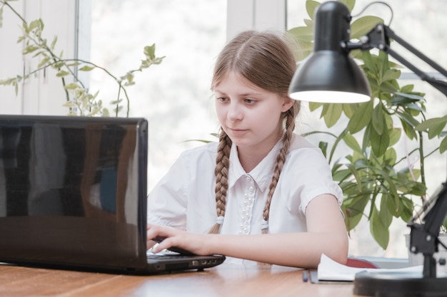 Mooi schoolmeisje dat huiswerk bestudeert tijdens haar online les thuis, sociale afstand tijdens quarantaine, zelfisolatie, online onderwijsconcept, thuisschooler. Online onderwijs op afstand