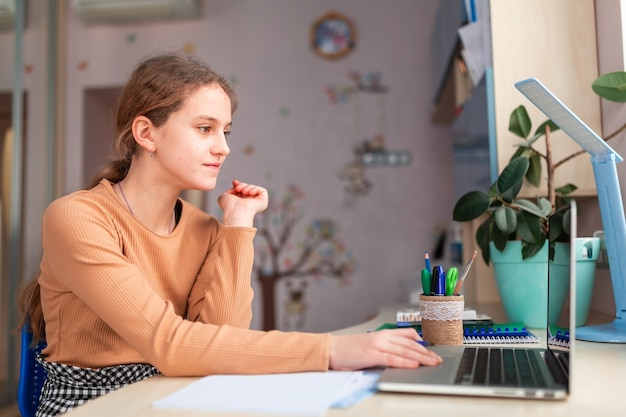 Mooi schoolmeisje dat thuis studeert en schoolthuiswerk doet. Trainingsboeken en notitieboekje op tafel. Online onderwijs op afstand