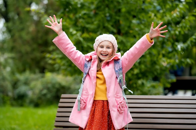 Mooi schoolmeisje met rugzak die naar de camera kijkt en handen vasthoudt en glimlacht in het herfstpark b