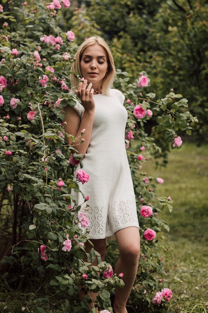 Mooi sexy meisje in wit gebreid op een achtergrond van natuur en bloeiende rozen