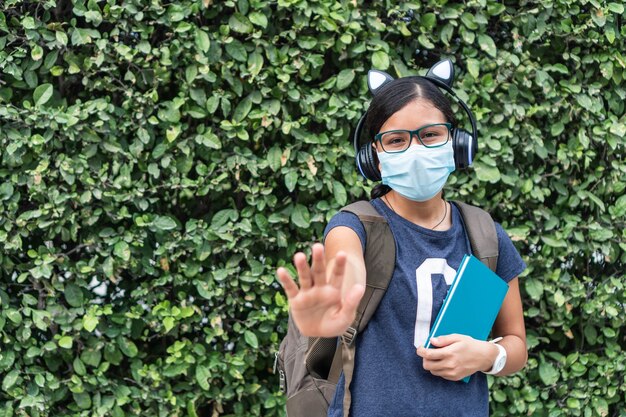 Mooi studentenmeisje met beschermend masker en rugzak met boeken met open hand die detentie aangeeft