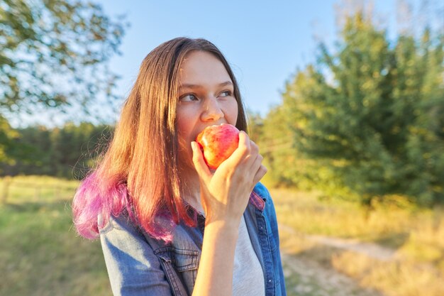 Mooi tienermeisje dat rijpe sappige smakelijke rode appel buiten eet. Mooie natuurlijke landschapsachtergrond, gouden uur. Natuurlijke gezonde voeding