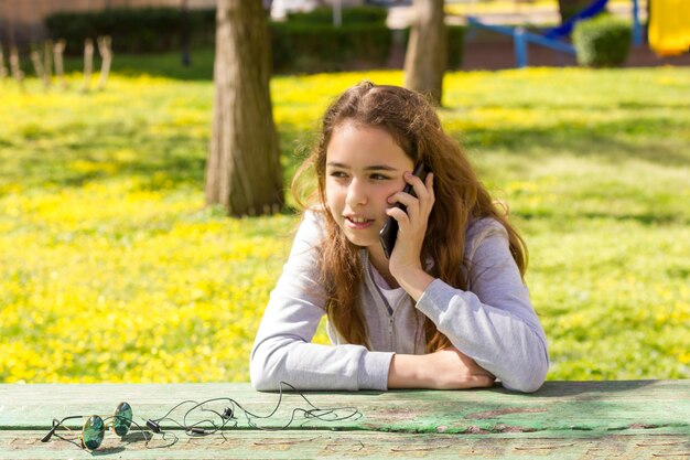 Mooi tienermeisje die door mobiele cellpfone smartphone bij het de zomerpark spreken