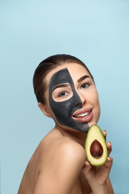 Mooi van lachende vrouw met gezichtsmasker op haar gezicht met een halve avocado Schoonheid Huidverzorging