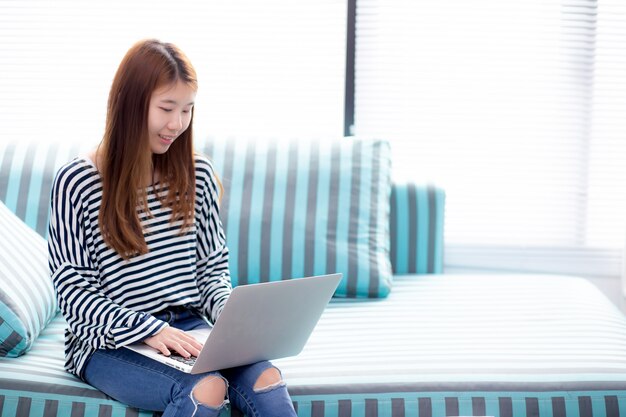 Mooi van portret Aziatische vrouw met behulp van laptop voor vrije tijd op de sofa