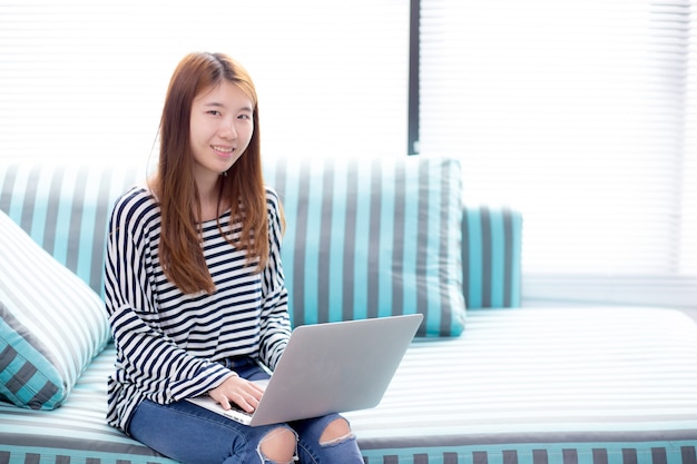 Mooi van portret jonge aziatische vrouw met behulp van laptop voor vrije tijd op de sofa