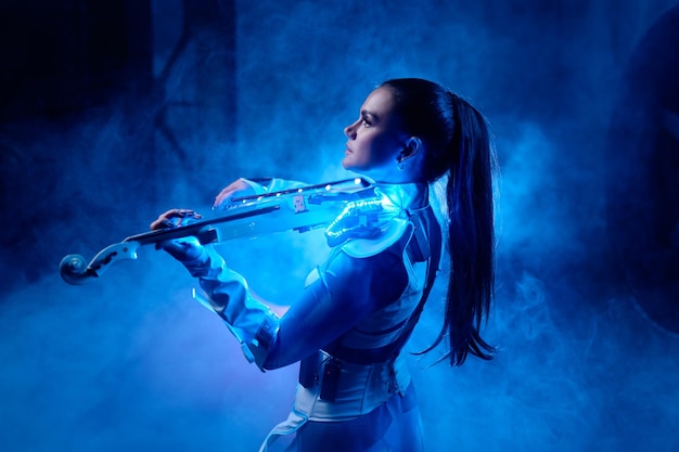 Mooi violiste meisje dat elektrische viool speelt op het podium met neonlicht en rook. Geïnspireerd vrouw muzikant portret. Prestaties van professionele artiesten