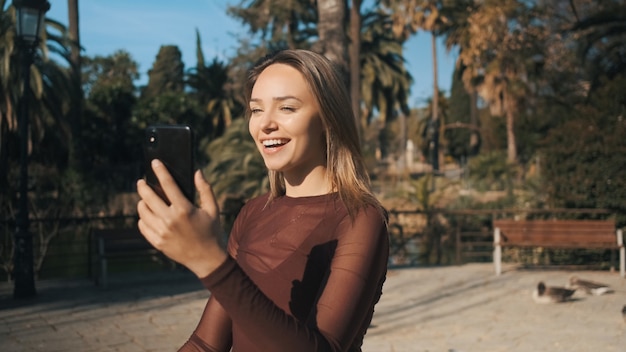 Mooi vrolijk meisje met behulp van smartphone gelukkig praten met vrienden op videochat tijdens het wandelen