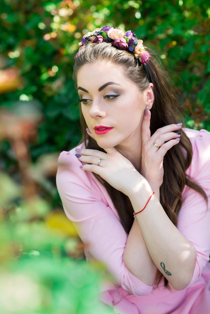 Mooi vrouwelijk model gekleed in een lange roze jurk poseert tussen de vele bloemen in de kas