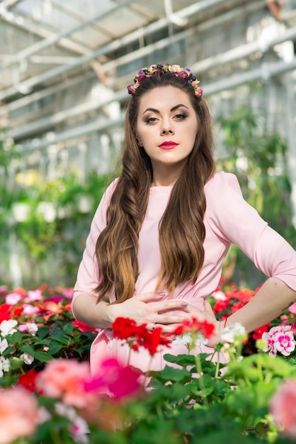 Mooi vrouwelijk model gekleed in een lange roze jurk poseert tussen de vele bloemen in de kas