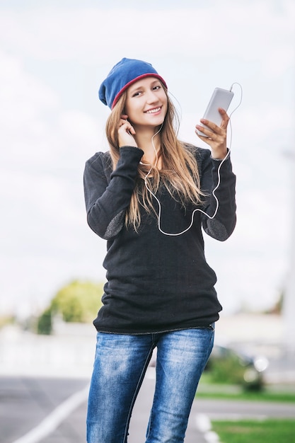 Mooi vrouwenmodel met telefoon en hoofdtelefoon die muziek in de straat luisteren