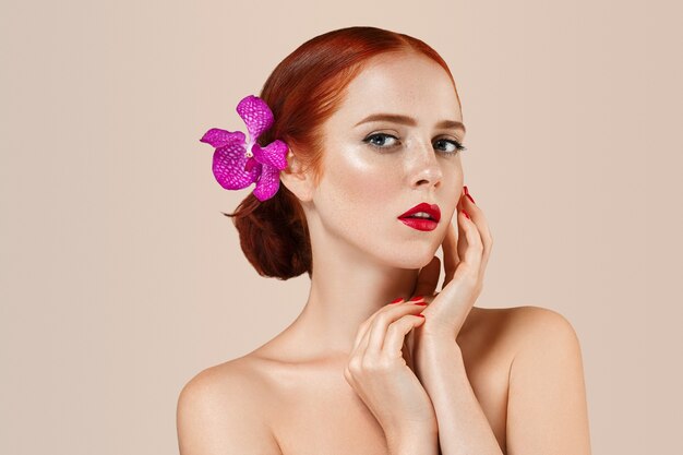 Mooi vrouwenportret met bloem in haar. perfecte make-up manicure rode lippen en nagels. Beige achtergrond