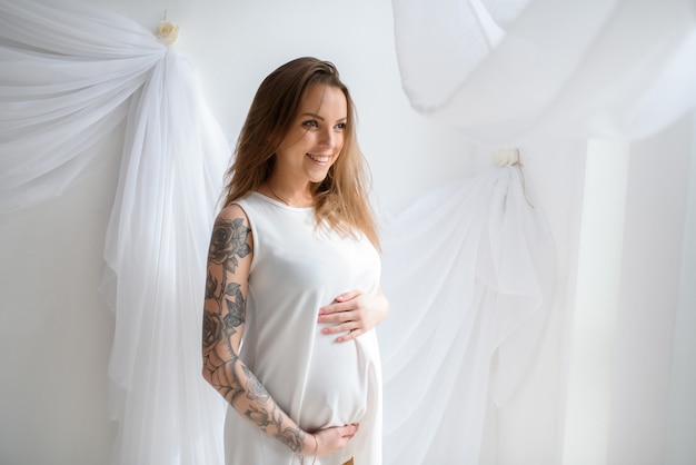 Mooi zwanger meisje met tatoeage in witte jurk.