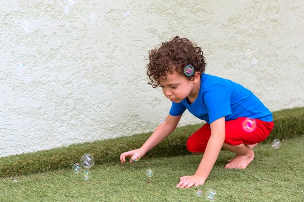 Mooie 4-5 jaar oude blanke jongen met krullend haar in zijn achtertuin spelen met zeepbellen