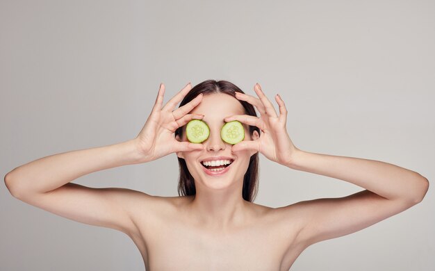 Mooie aantrekkelijke jonge dame met haar met volle lippen en een speelse bui. De vrouw maakte glazen van plakjes komkommer en glimlachte met witte tanden. spa, cosmetica. Midden frame