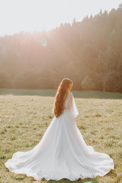 Mooie achterkant van de bruid in een trouwjurk op het veld bij de zonsondergang