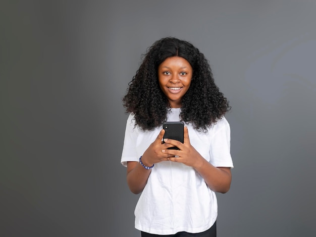 Mooie Afrikaanse tienerdame die mobiele telefoon vasthoudt en naar de camera kijkt