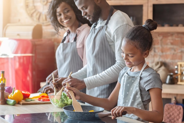 Mooie Afrikaanse veganistische familie die samen een gezond diner maakt, dochter leert koken, ouders die salade maken, ruimte kopiëren