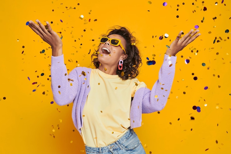 Foto mooie afrikaanse vrouw die confetti gooit en glimlacht tegen een gele achtergrond.