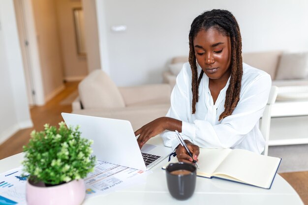 Mooie Afrikaanse vrouw freelancer die informatie opmerkt voor het plannen van een project dat op afstand werkt via een laptopcomputer. Vrouw die lacht tijdens het lezen van e-mail op een modern laptopapparaat