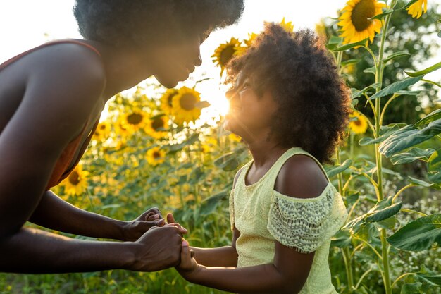 Mooie Afro-Amerikaanse moeder en dochter die spelen en plezier hebben in een zonnebloemveld