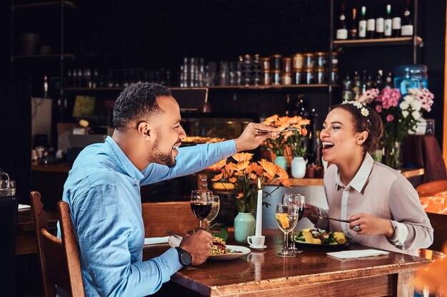 Mooie Afro-Amerikaanse verliefde paar hebben een geweldige tijd samen tijdens hun dating, een aantrekkelijk stel dat van elkaar geniet, knappe man die zijn vrouw voedt in een restaurant.