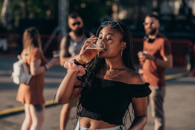 Mooie Afro-Amerikaanse vrouw die bier drinkt en plezier heeft op muziekfestival