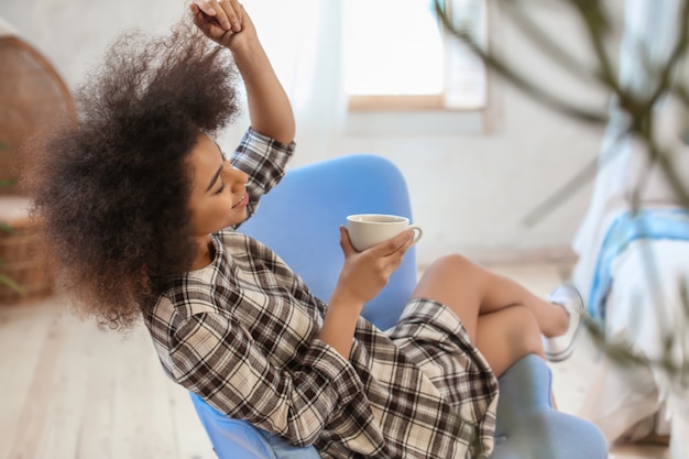 Mooie Afro-Amerikaanse vrouw die thuis thee drinkt in een leunstoel