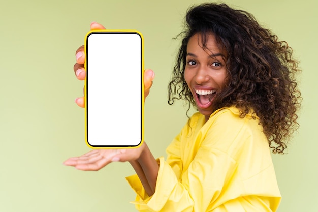 Mooie Afro-Amerikaanse vrouw in casual shirt op groene achtergrond houdt een telefoon met een lege whit