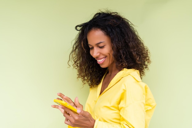 Mooie afro-amerikaanse vrouw in casual shirt op groene achtergrond houdt mobiele telefoon met een glimlach